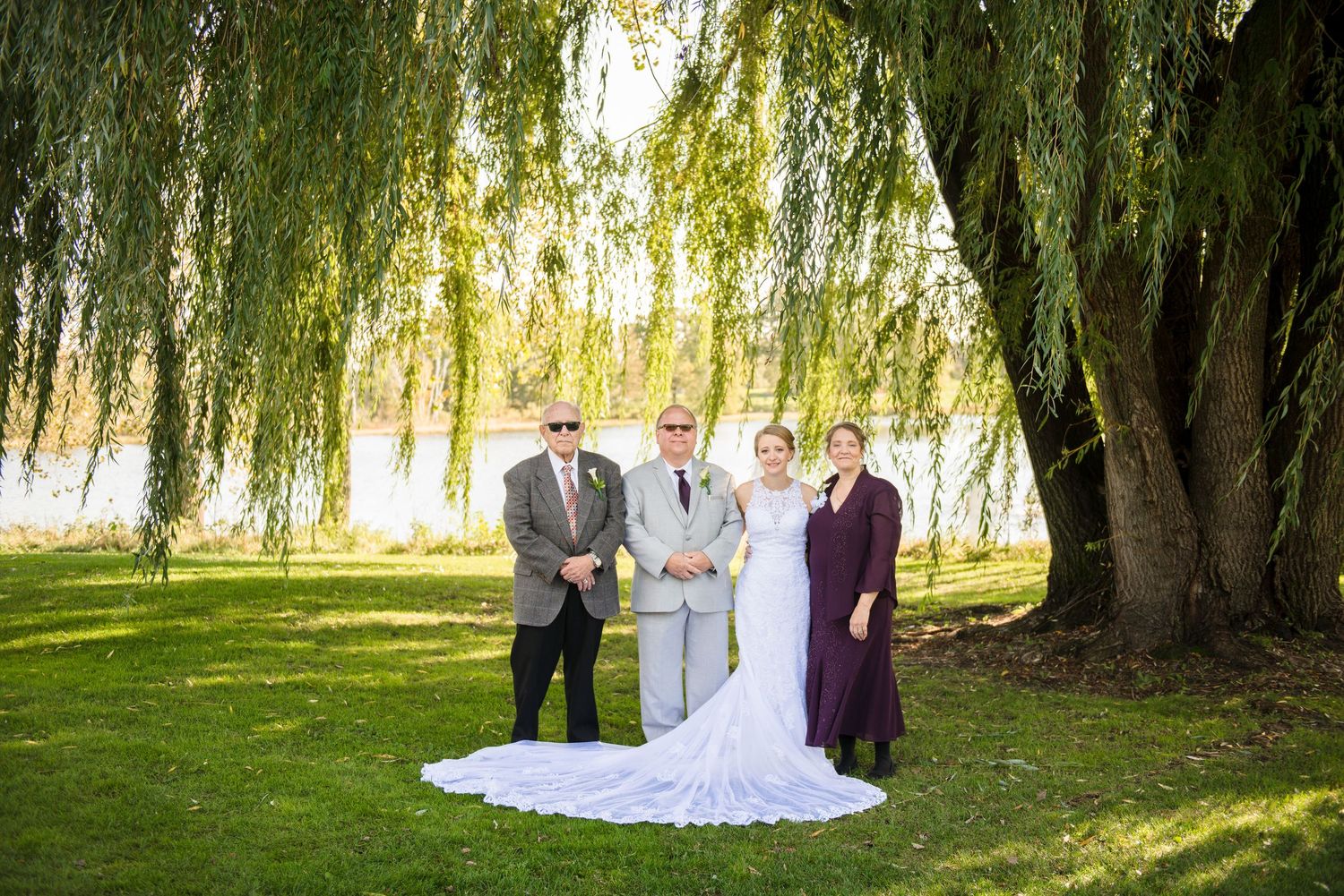 Wedding party poses under a large weeping willow tree beside a lake. Andover wedding at Magestic Oaks Golf Club
