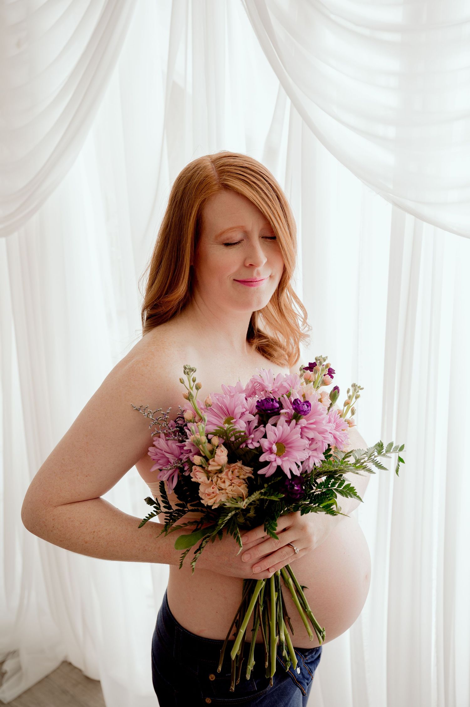 Woman in black top holds romantic bouquet of pink and purple flowers against white curtained background.