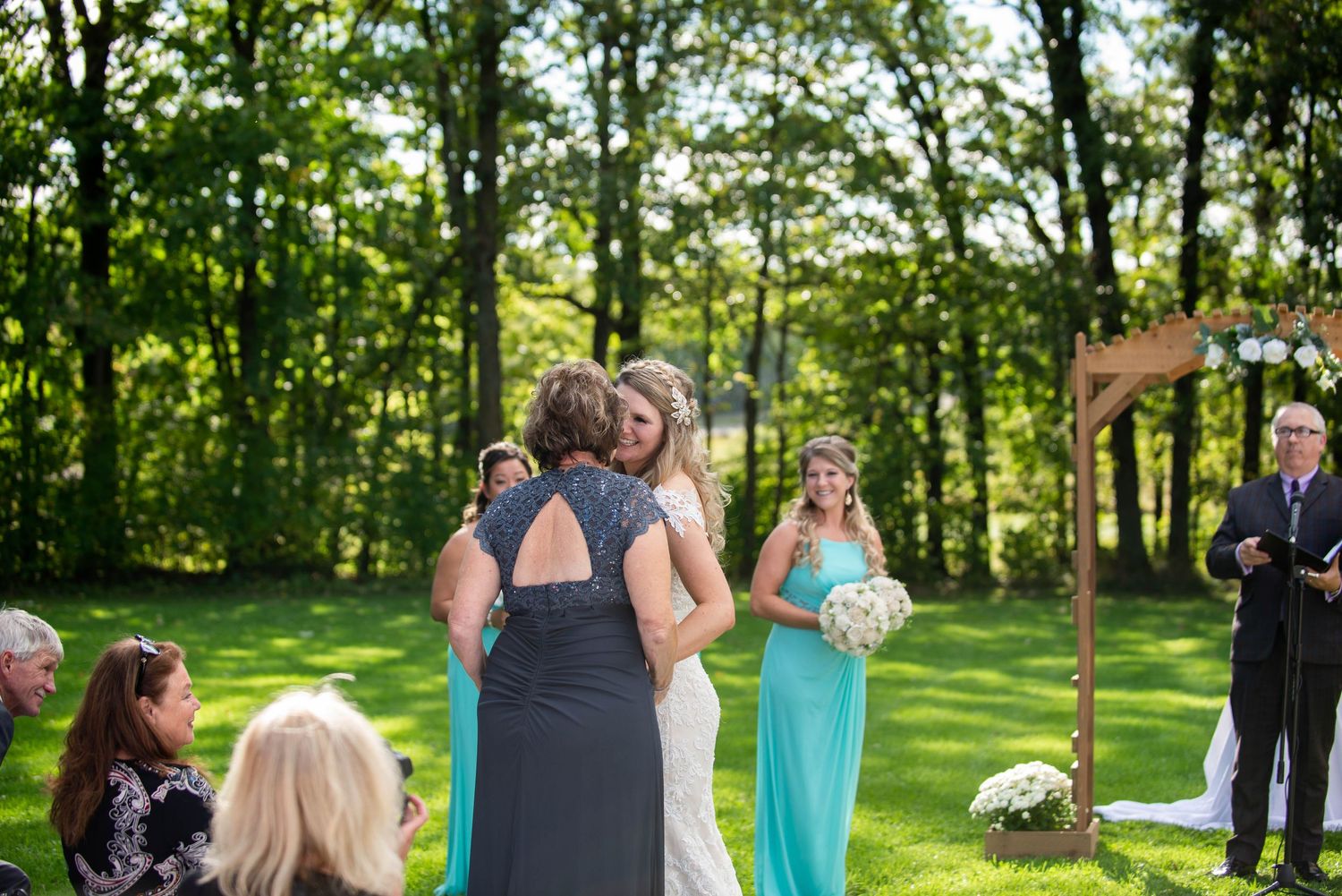 Outdoor wedding ceremony in progress with guests seated in a wooded setting. Rum River Barn Milaca Minnesota Weddings