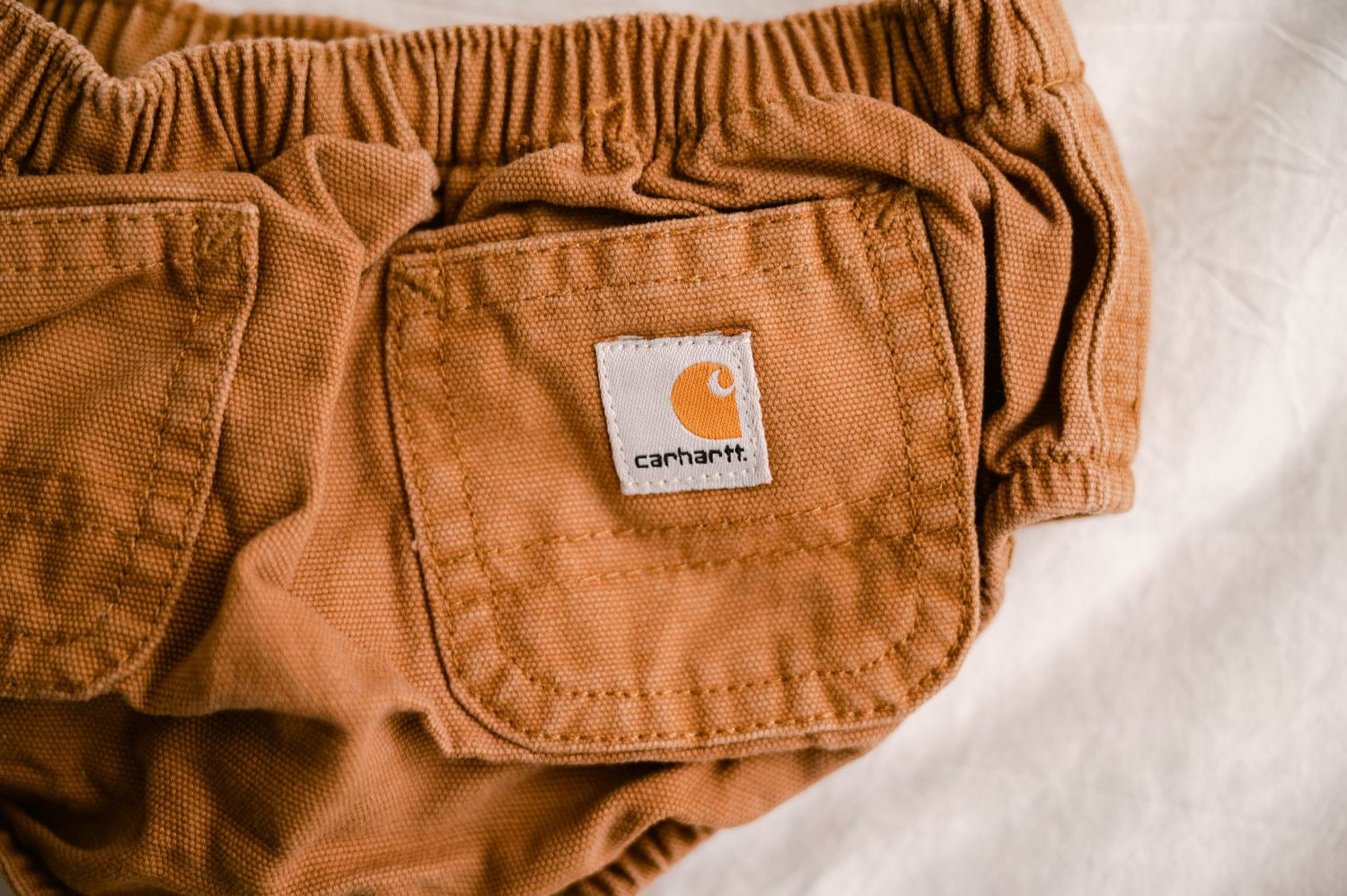 Close up of a brown Carhartt pants pocket with signature brand patch label on white background.