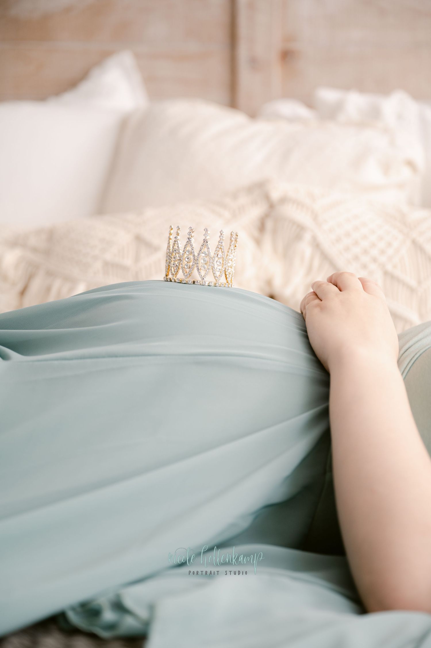 A delicate crown rests on a light blue fabric against white bedding, creating a dreamy and romantic composition.