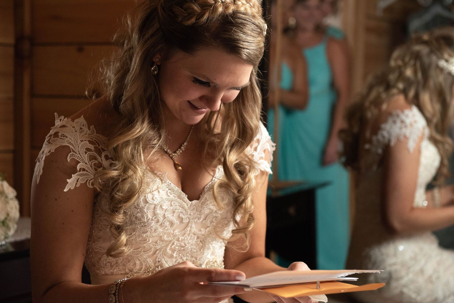 Bride wearing lacy cap sleeve wedding dress smiles while looking at tablet device during wedding preparations.