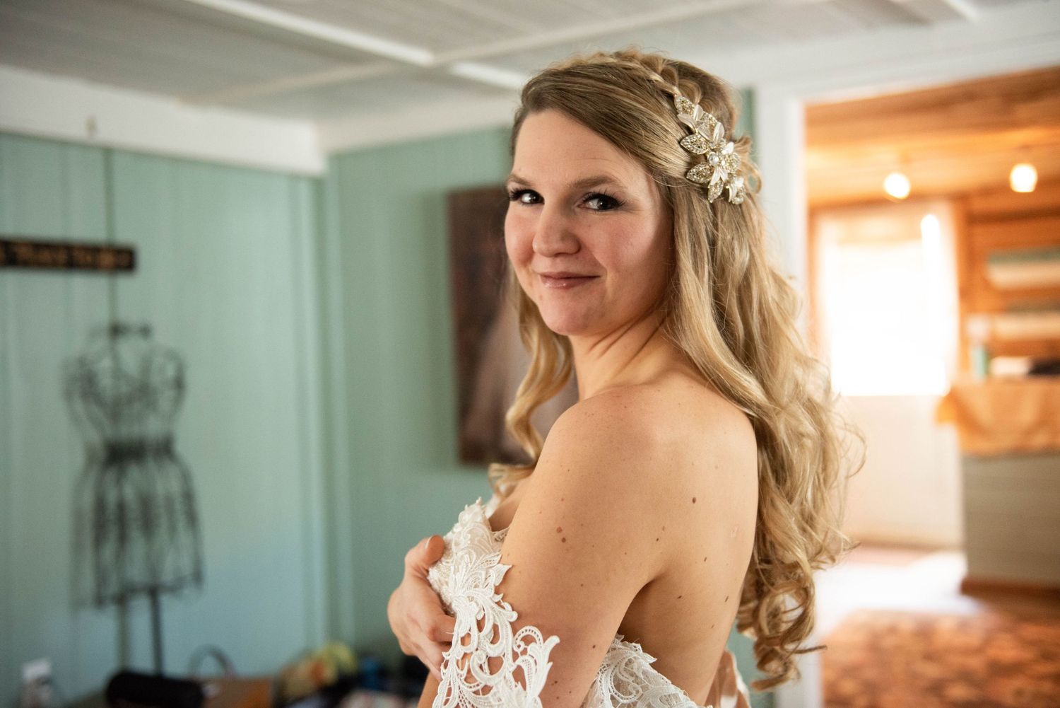 A bride in a lace strapless gown and floral headpiece poses in a mint-colored room.