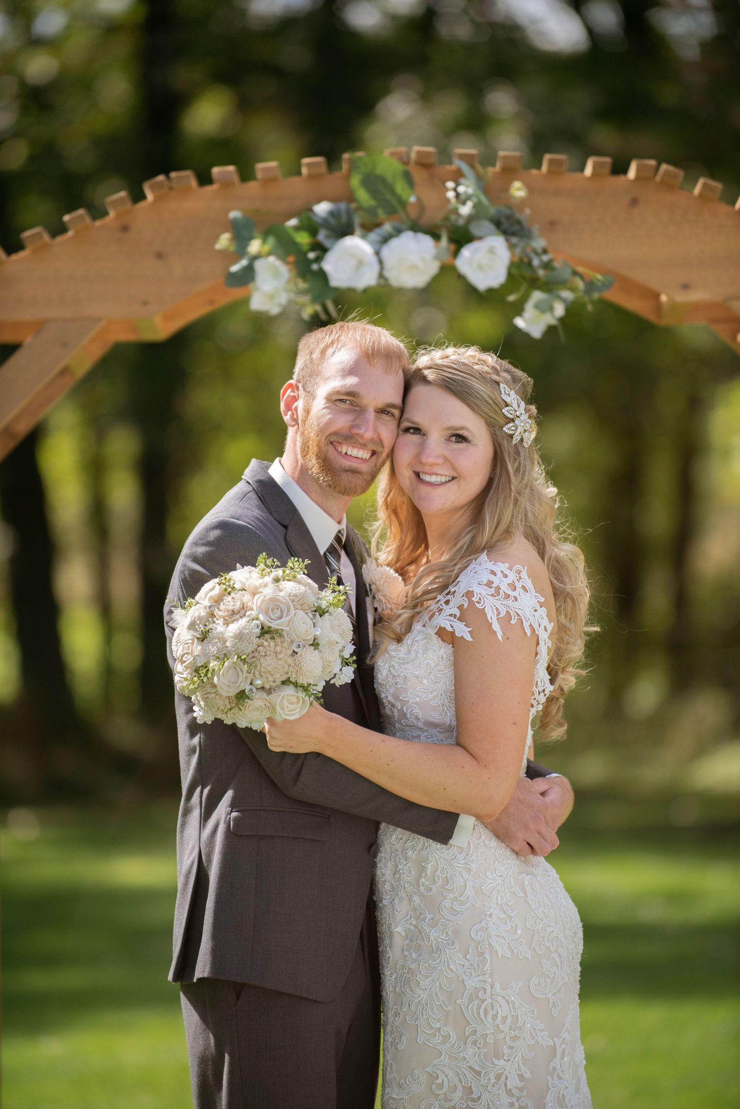 A romantic wedding portrait under a wooden arch decorated with white flowers in a garden setting. Rum River Barn Milaca Minnesota Weddings