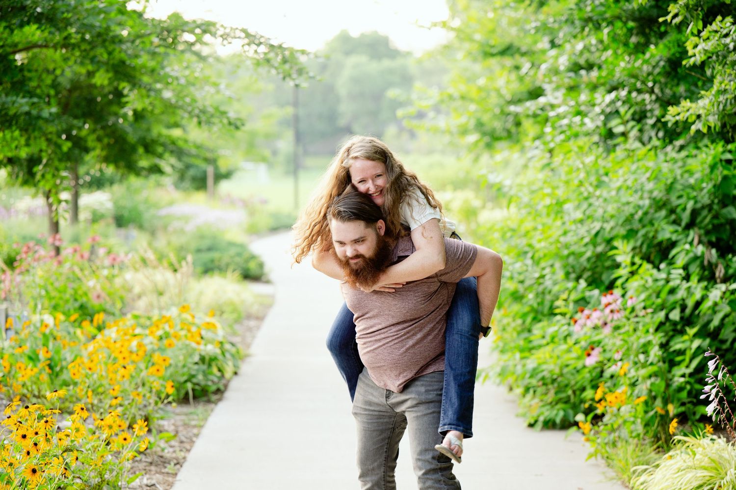 A playful piggyback ride along a garden path lined with vibrant yellow wildflowers and lush greenery.