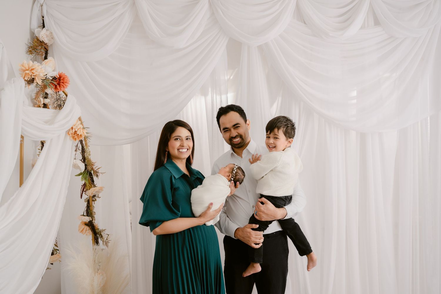 Family photo session with floral decorations and white draped backdrop.