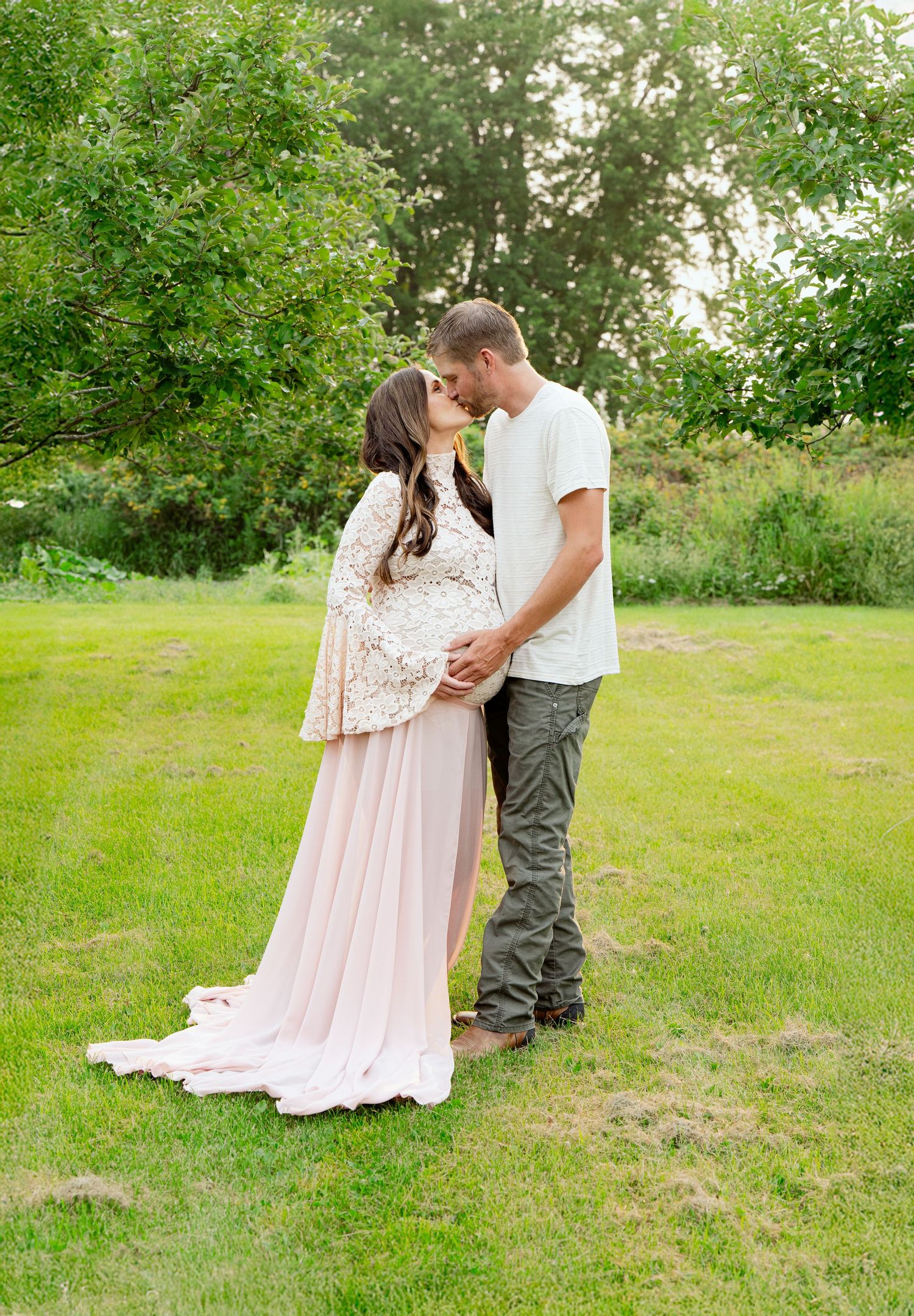 Romantic maternity photo of couple in garden with flowing pink dress.