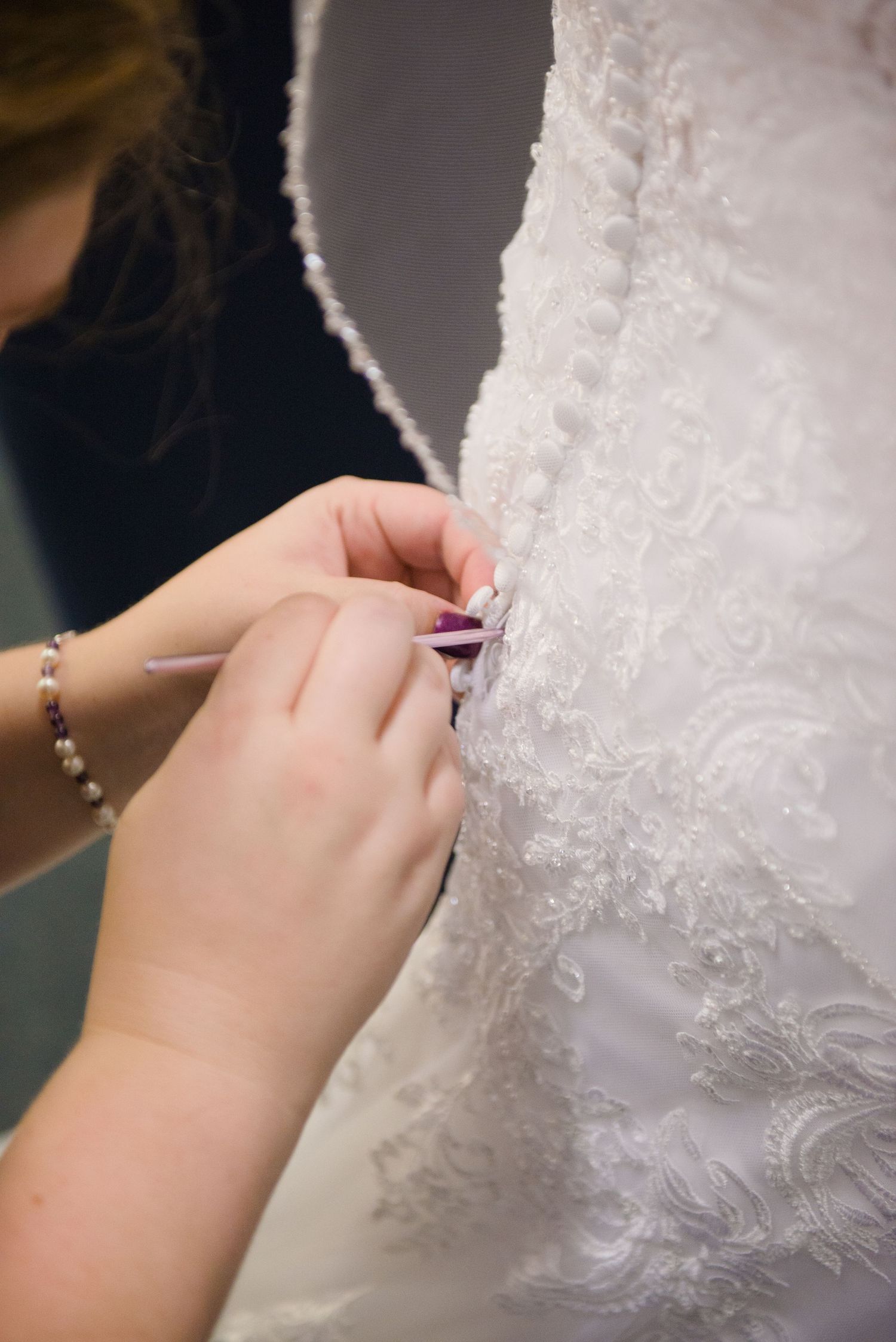 Close-up of hands delicately adjusting the intricate lace details on a white wedding dress. Andover wedding at Magestic Oaks Golf Club