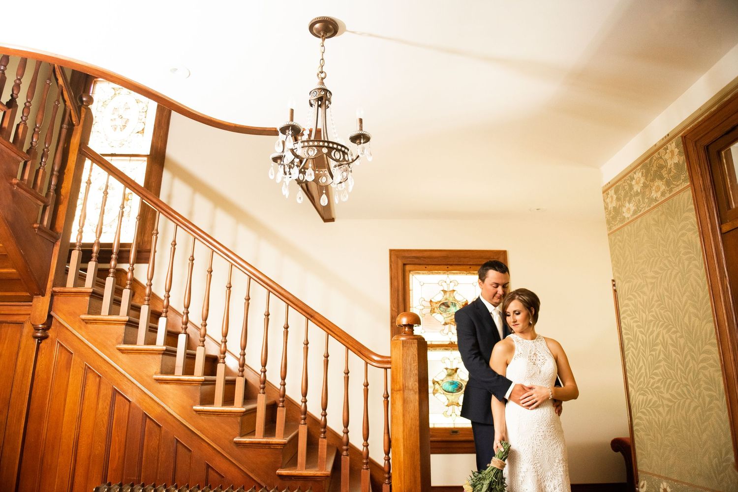 A couple shares a tender moment on their wedding day in an elegant stairwell with warm lighting.