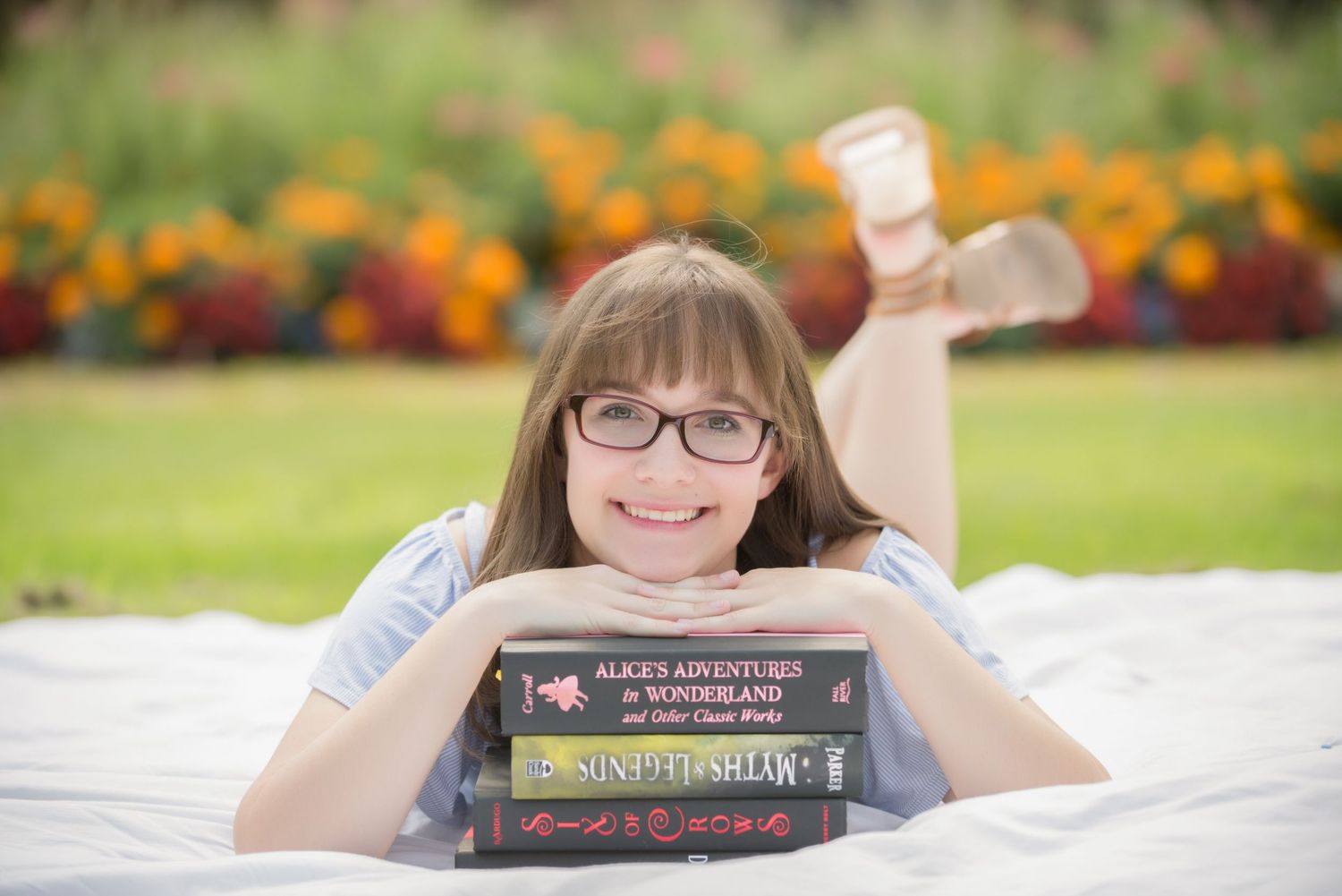 Senior Portrait at St Cloud State CollegeA reading series with books displayed on white bedding against a colorful floral garden background.