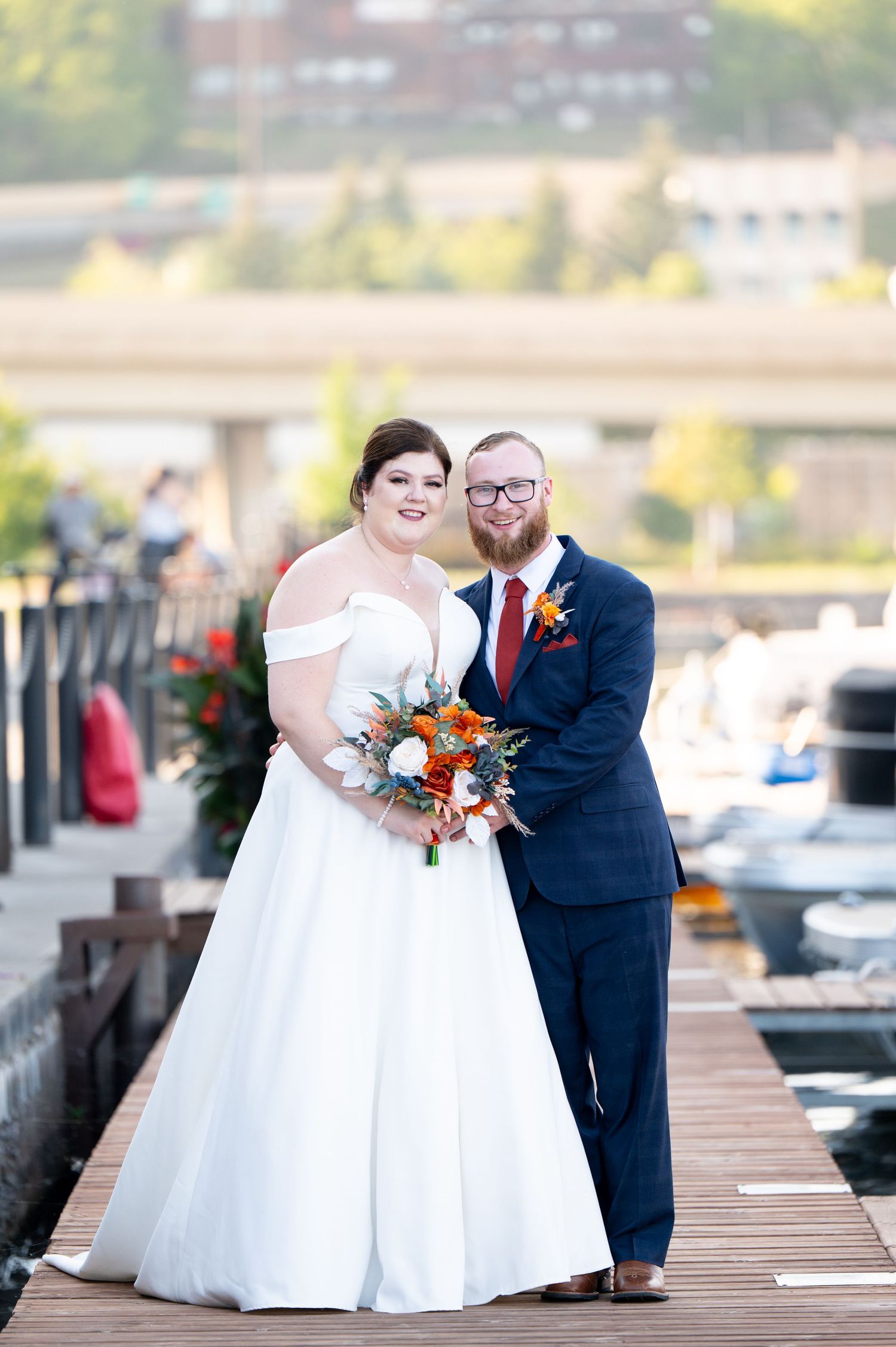 Pier B Duluth Wedding Newlyweds pose for portraits on wooden dock with marina and autumn scenery in background.