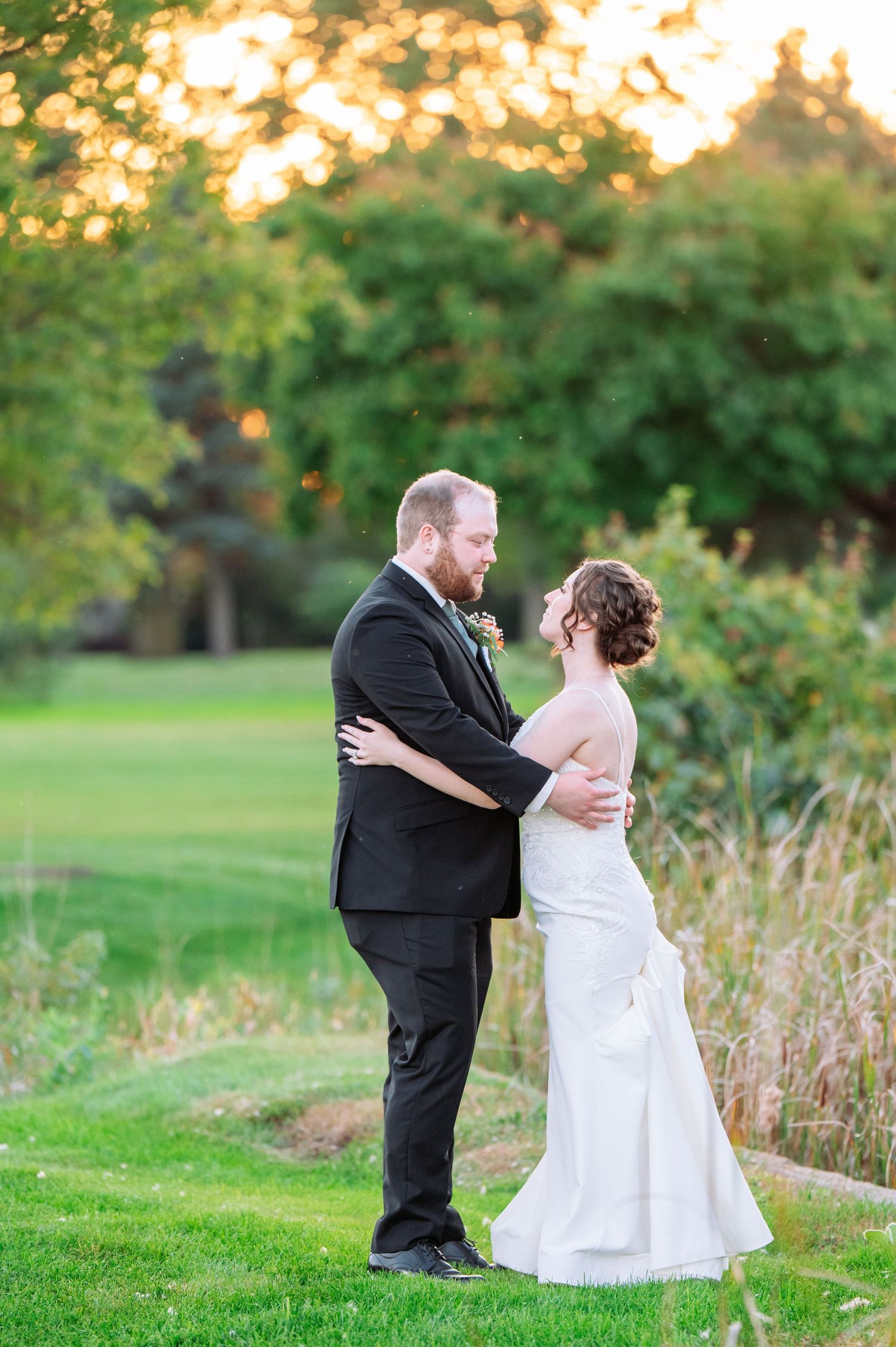 The Grands at Mulligans- Wedding Photos: showing playful poses of a couple in formal attire on a grassy lawn at sunset.