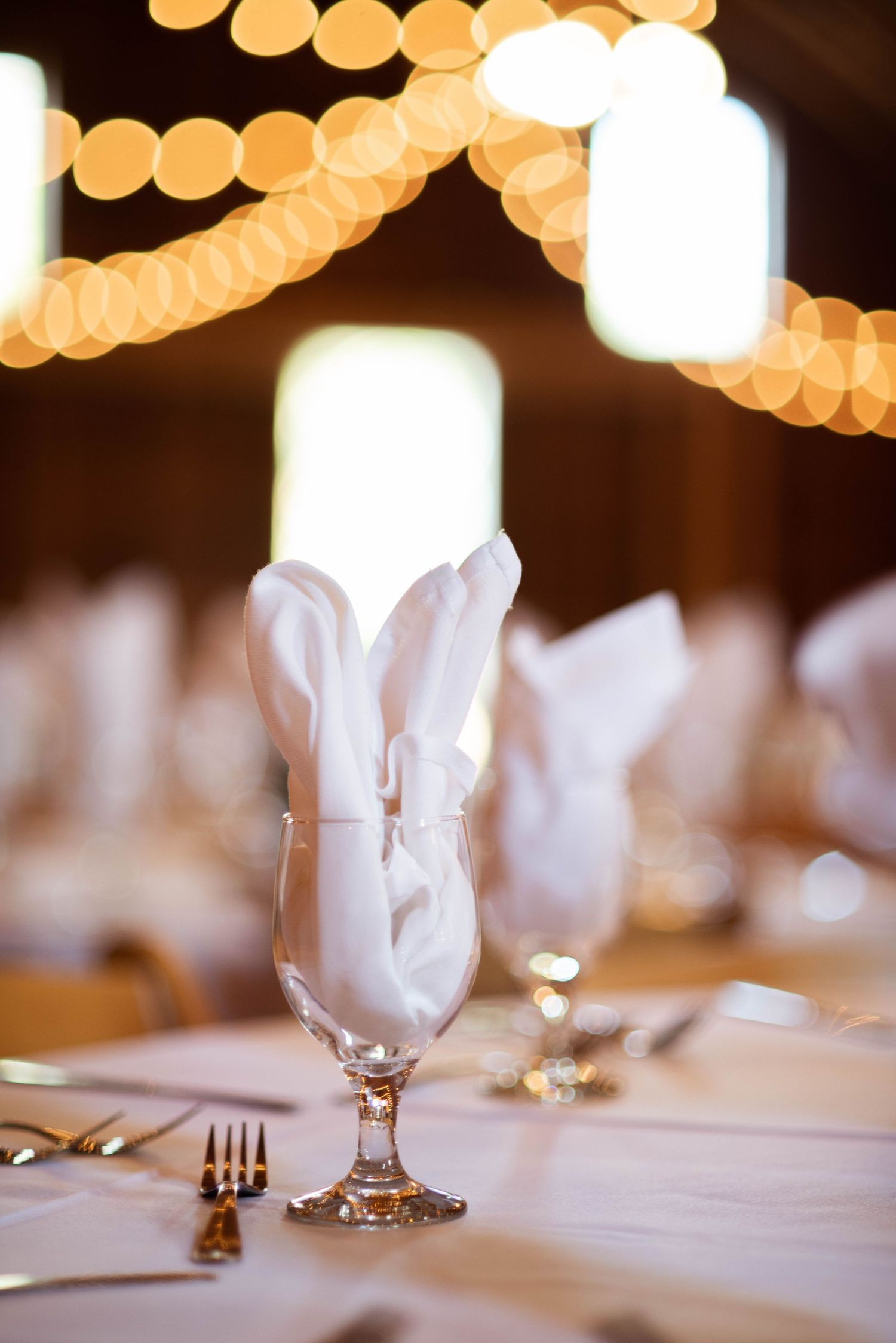 White table settings and wine glasses with warm bokeh lights creating an elegant reception ambiance.