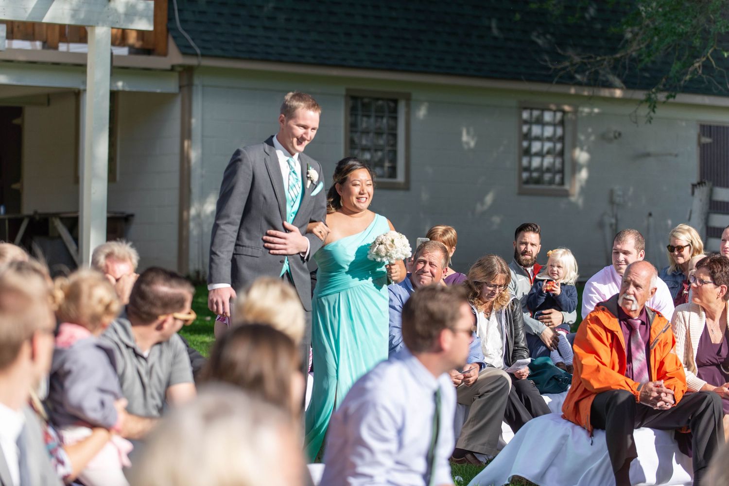 Wedding guests watch a ceremony procession outdoors on a sunny day. Rum River Barn Milaca Minnesota Weddings