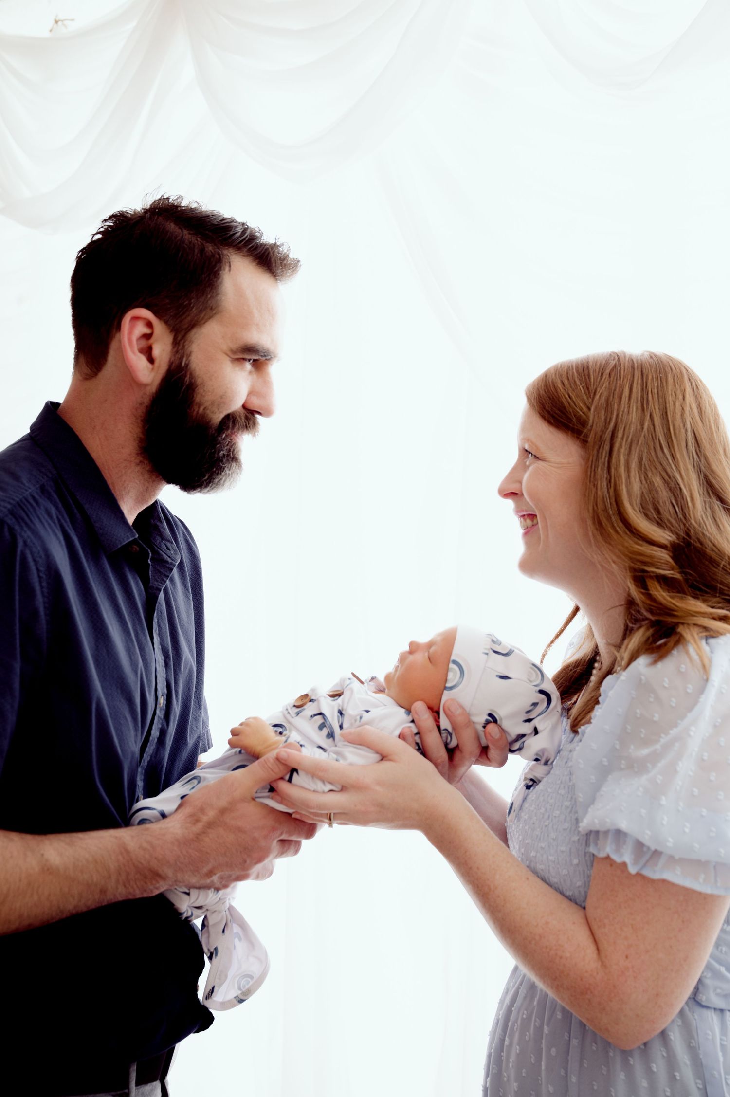 Joyful parents sharing tender moment with newborn baby against white background.