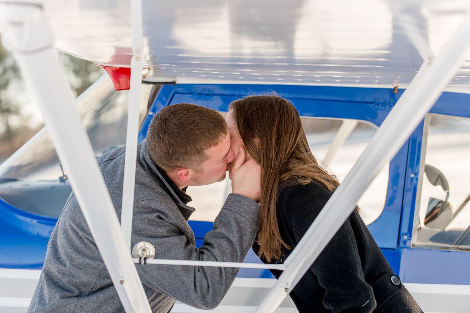 Couple embracing against a blue aircraft on a bright sunny day.