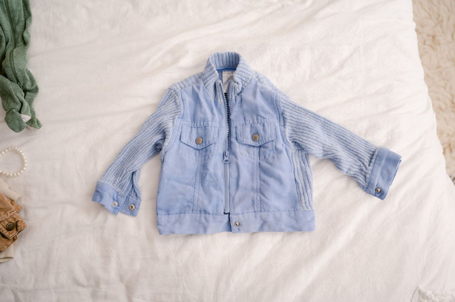 Light blue denim utility jacket with front pockets and zip closure laid flat on white background.