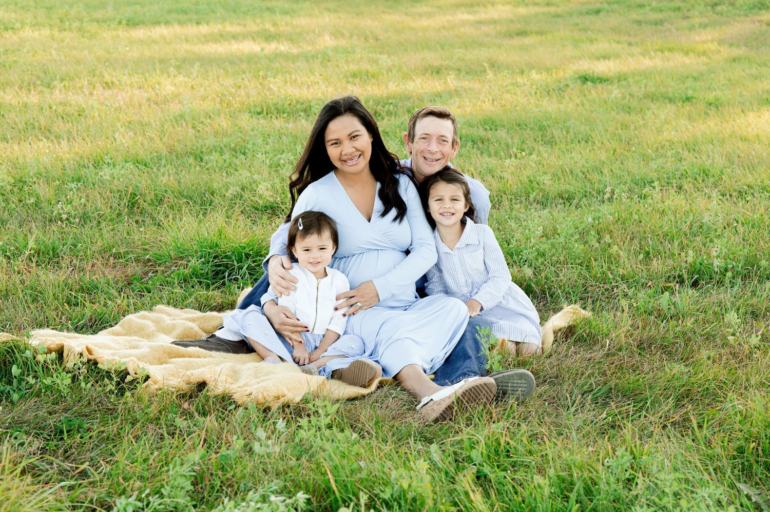 Family sitting together on picnic blanket in sunny grassy field.
