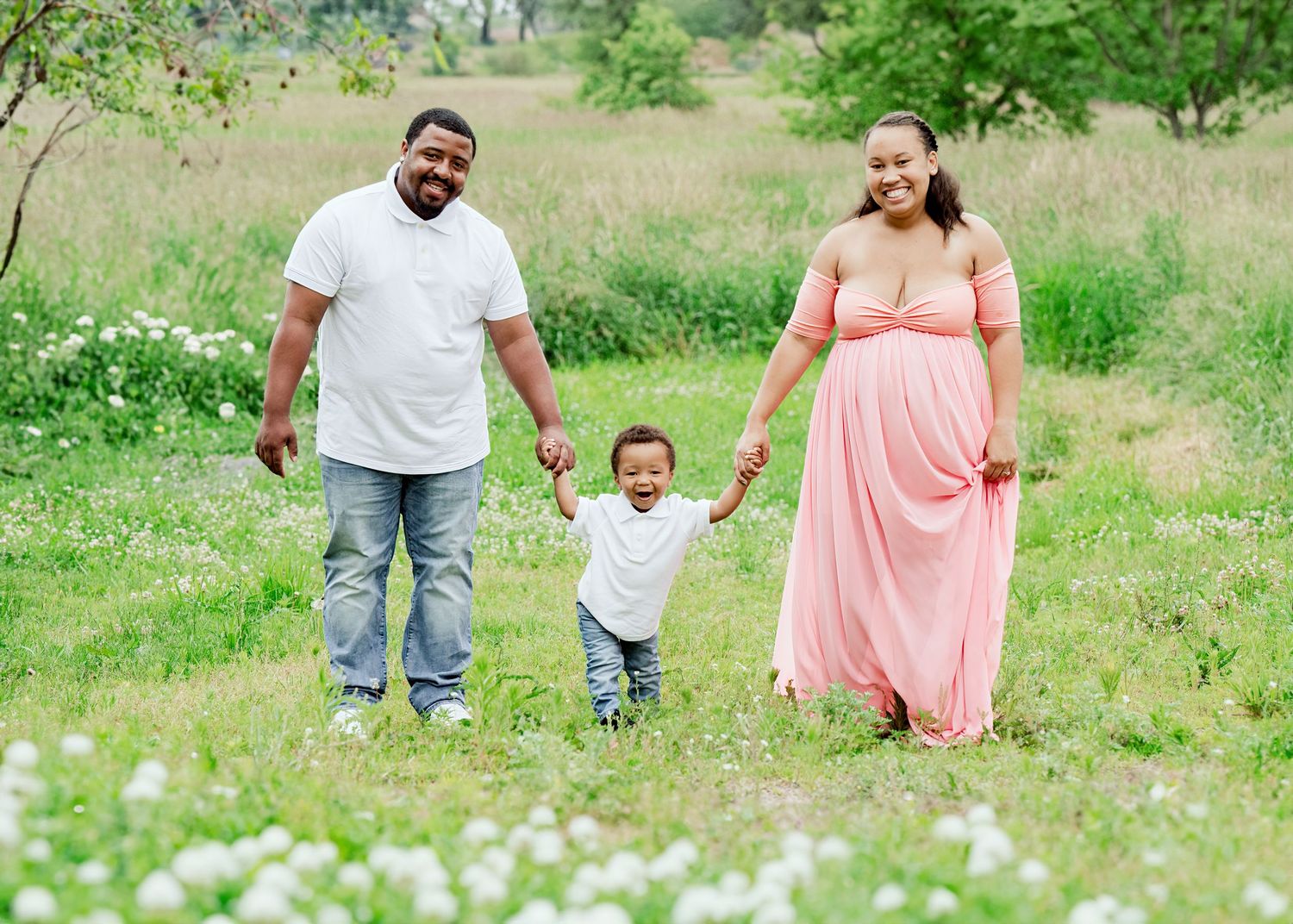 Family walks together through wildflower field during spring photo session.