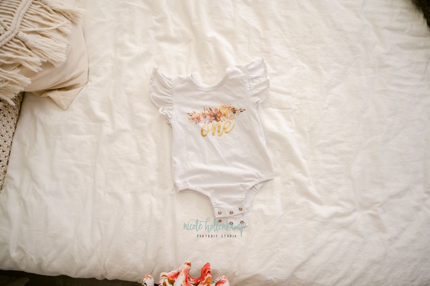 White t-shirt laying on a rumpled white bedspread with beige pillows in soft natural lighting.
