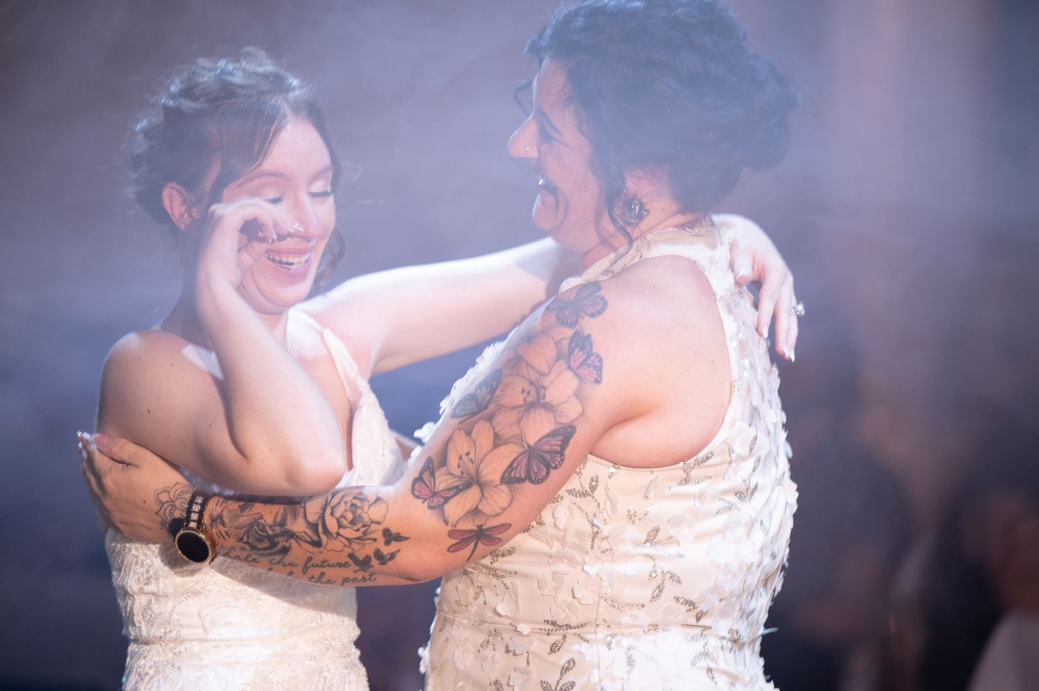Two brides in white dresses share a joyful moment together on their wedding day.