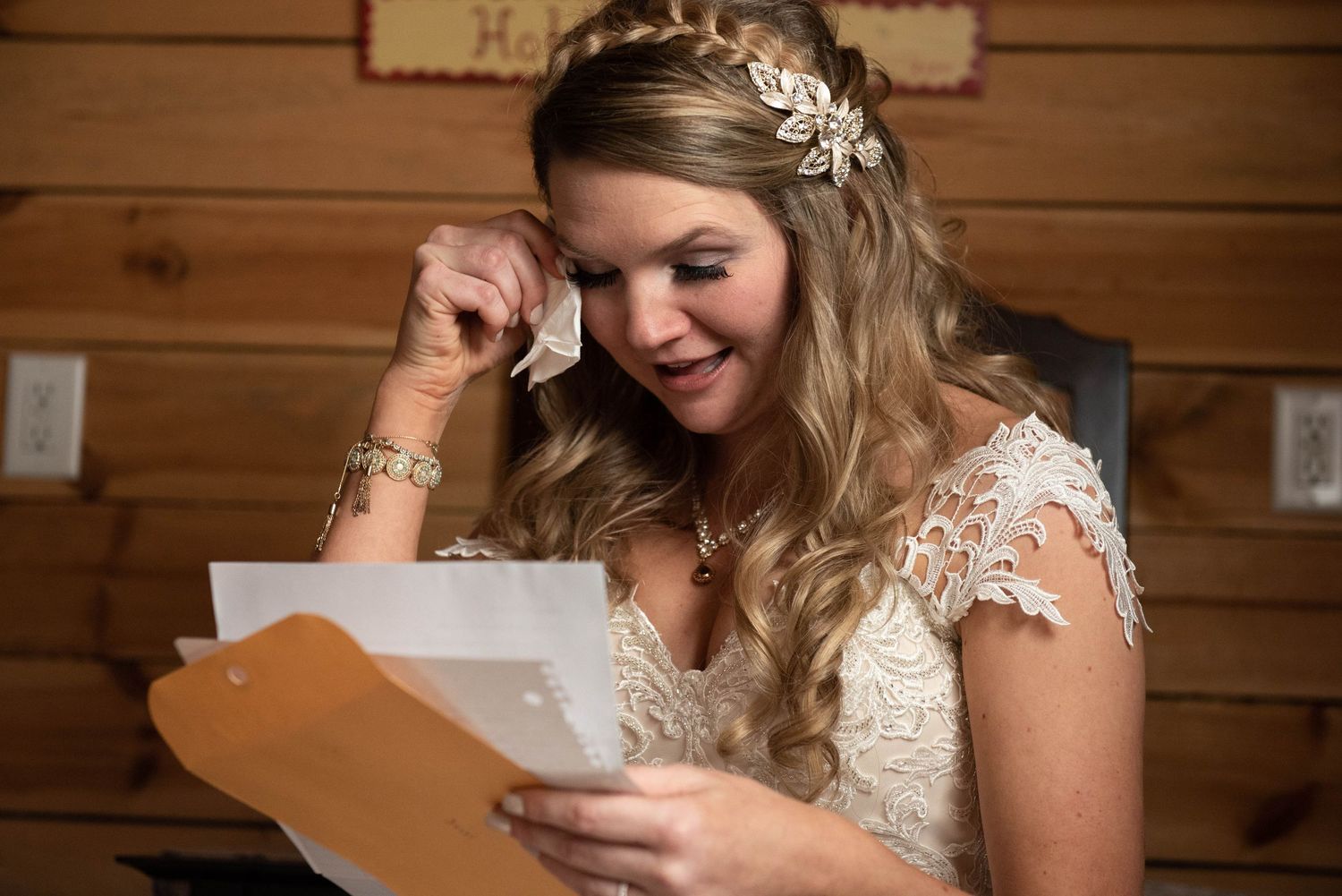 A bride in a white lace gown reads a letter in a rustic wooden cabin setting. Rum River Barn Milaca Minnesota Weddings