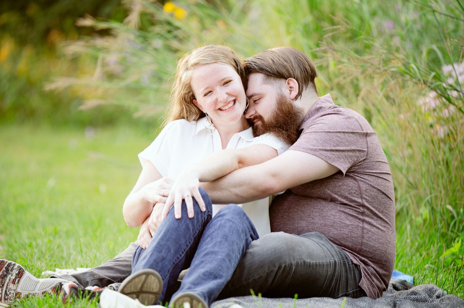 Intimate moment shared while sitting in grass surrounded by wildflowers on a sunny day.
