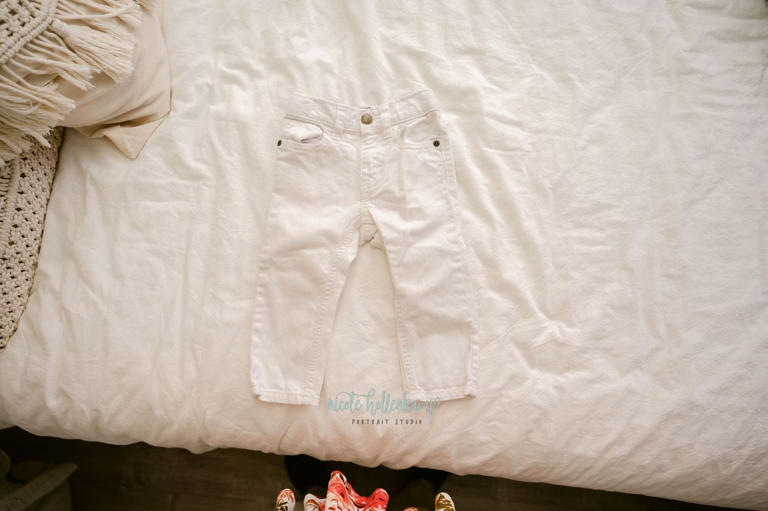 A white denim pants laid flat on a bed with a knitted sweater visible in the corner.