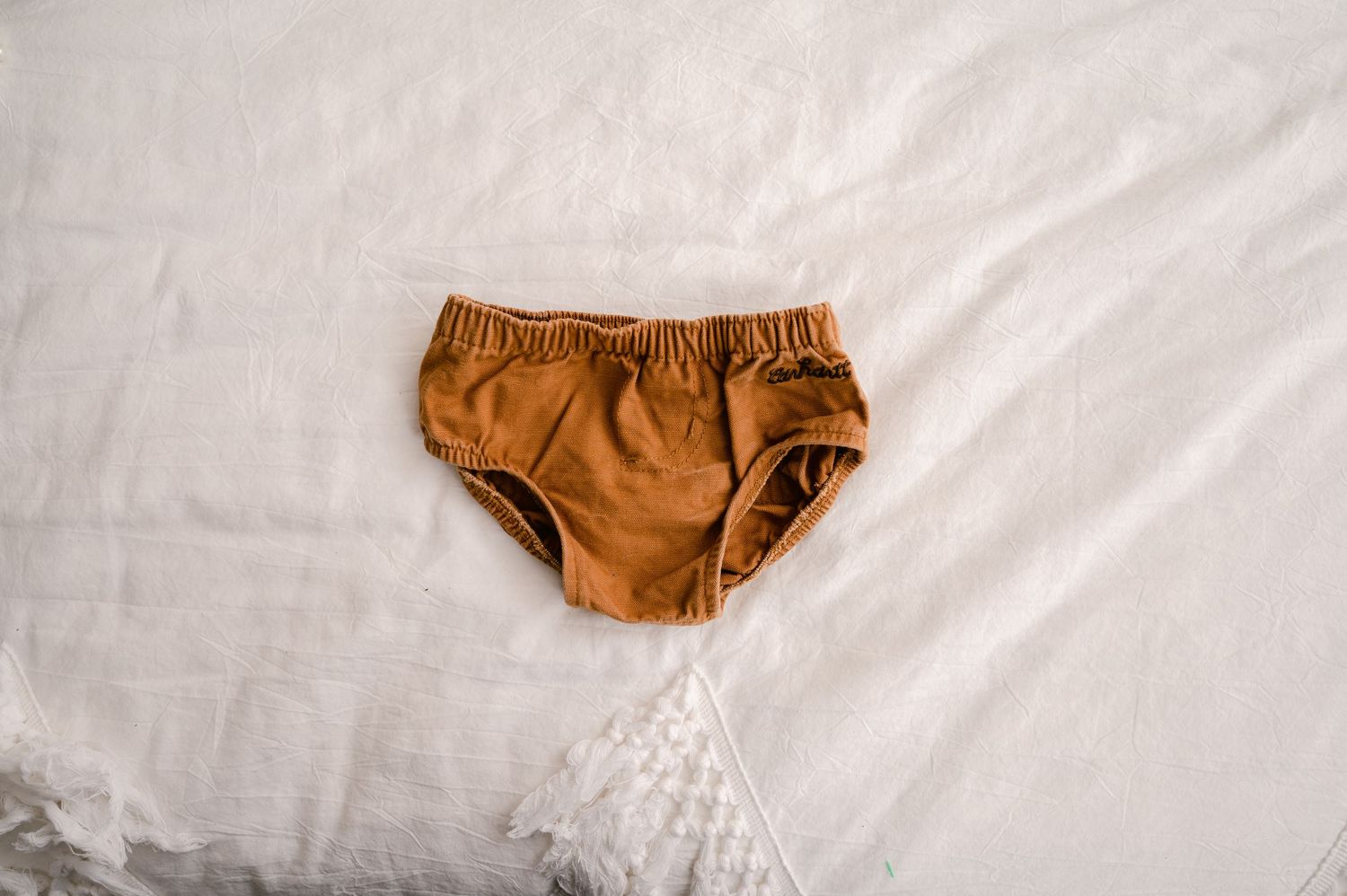 A brown toddler underwear or diaper cover lies on a white textured fabric background.