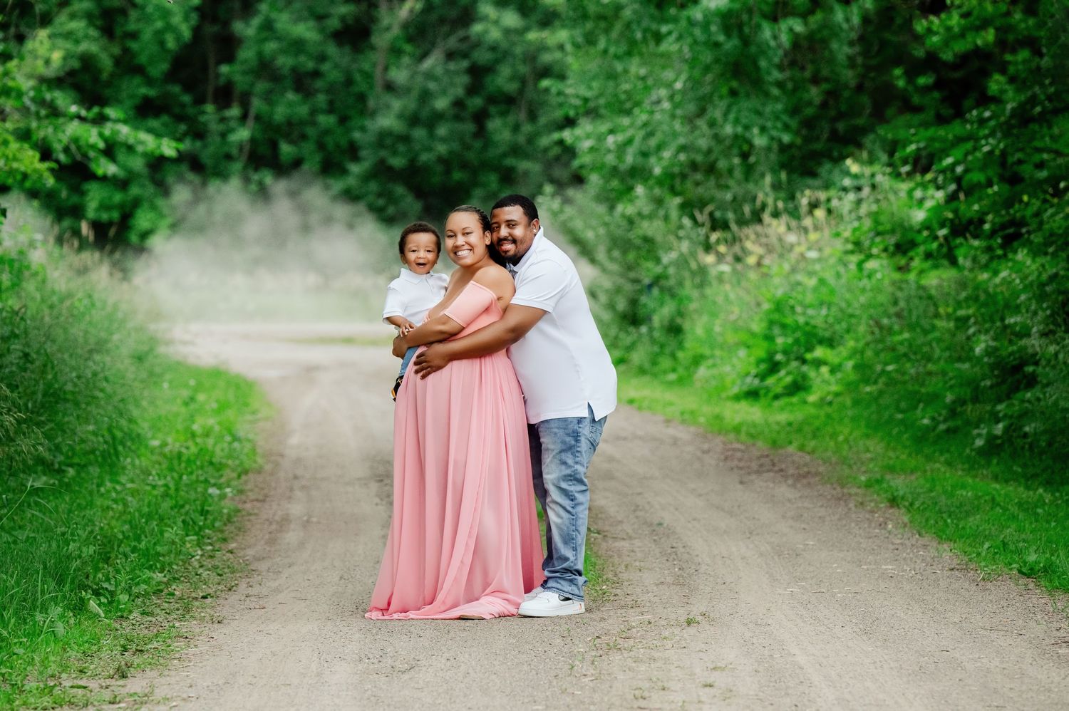 Family embracing on a dirt path surrounded by lush green foliage on a sunny day.