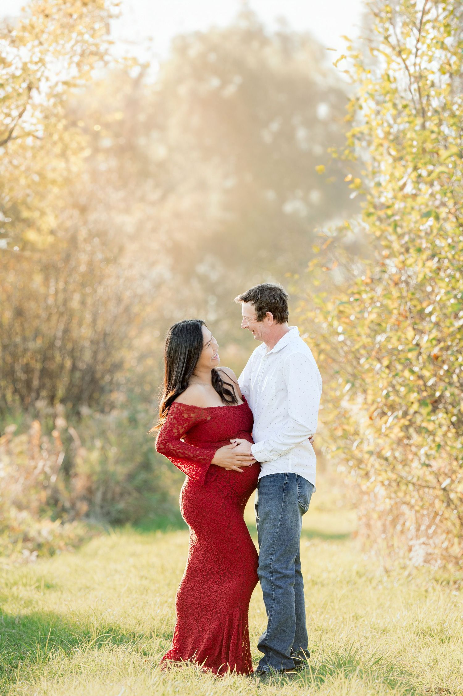 Couple embracing in autumn field with golden leaves and sunlight.