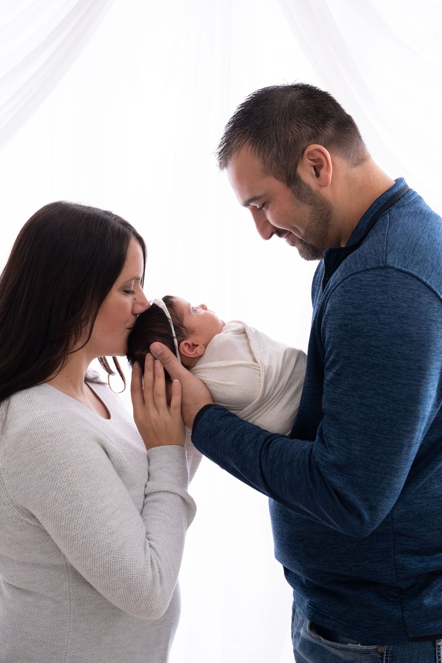 Parents in casual clothes tenderly holding and admiring their swaddled newborn.