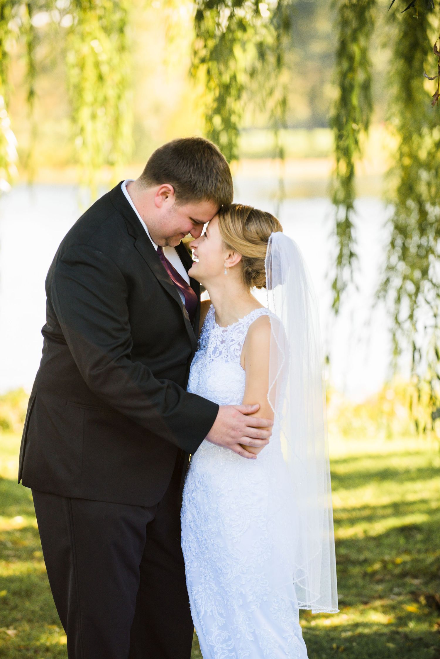 Romantic wedding portrait of couple embracing under a weeping willow tree on a sunny day. Andover wedding at Magestic Oaks Golf Club