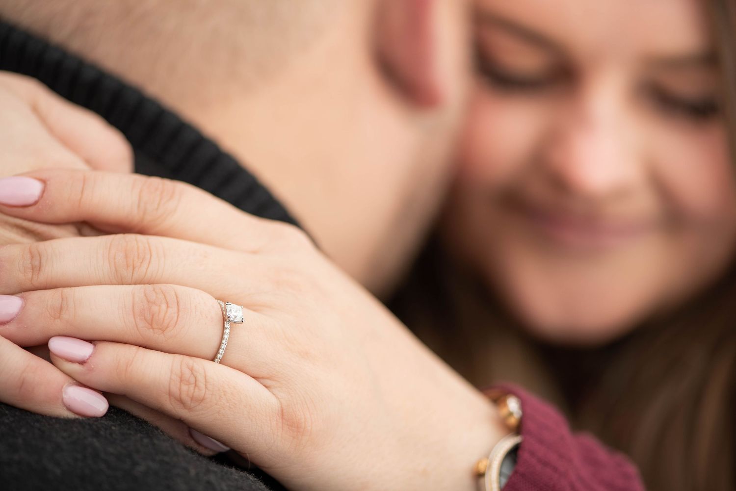 A close-up view of hands embracing with an engagement ring visible on a manicured finger.