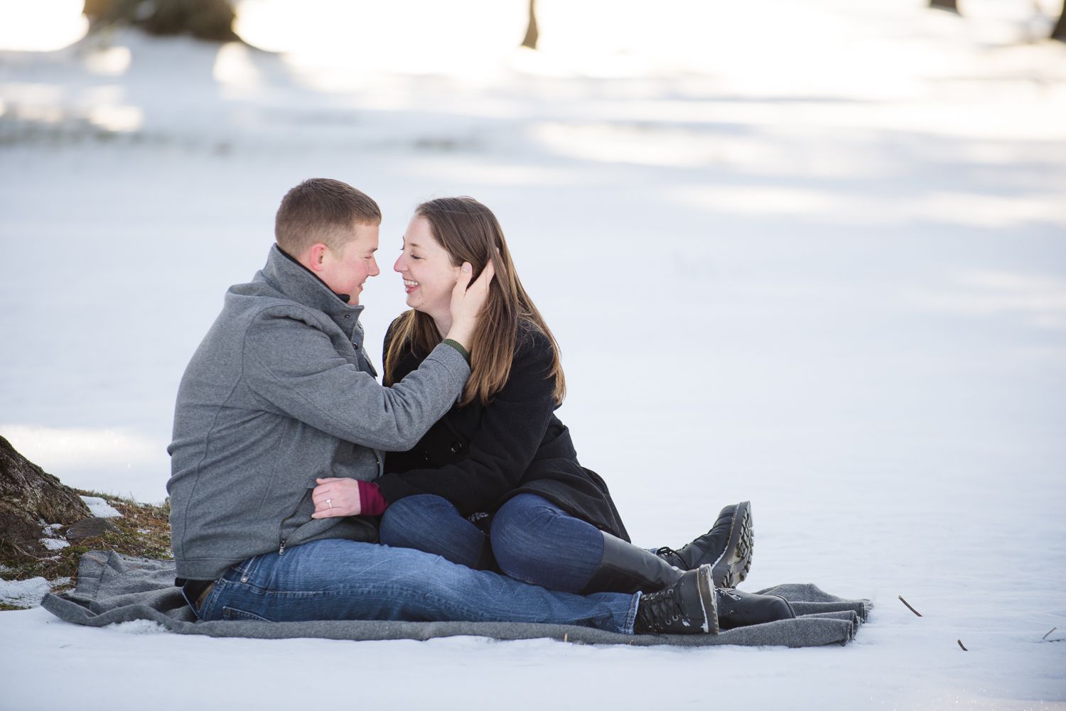 Romantic couple lying together on snowy ground during winter engagement photo shoot.