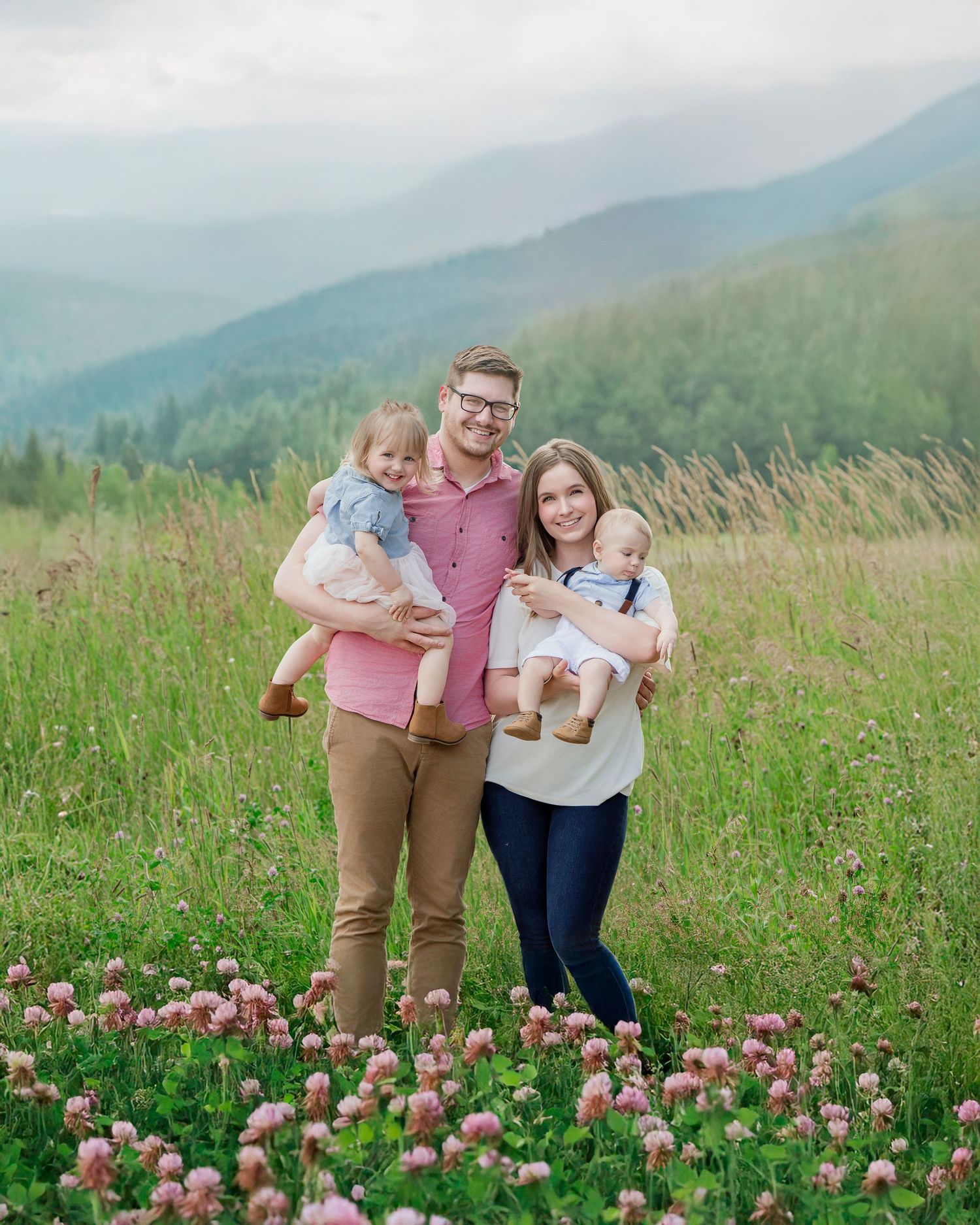 A family stands together in a wildflower meadow with pink blossoms and misty mountains in the background.