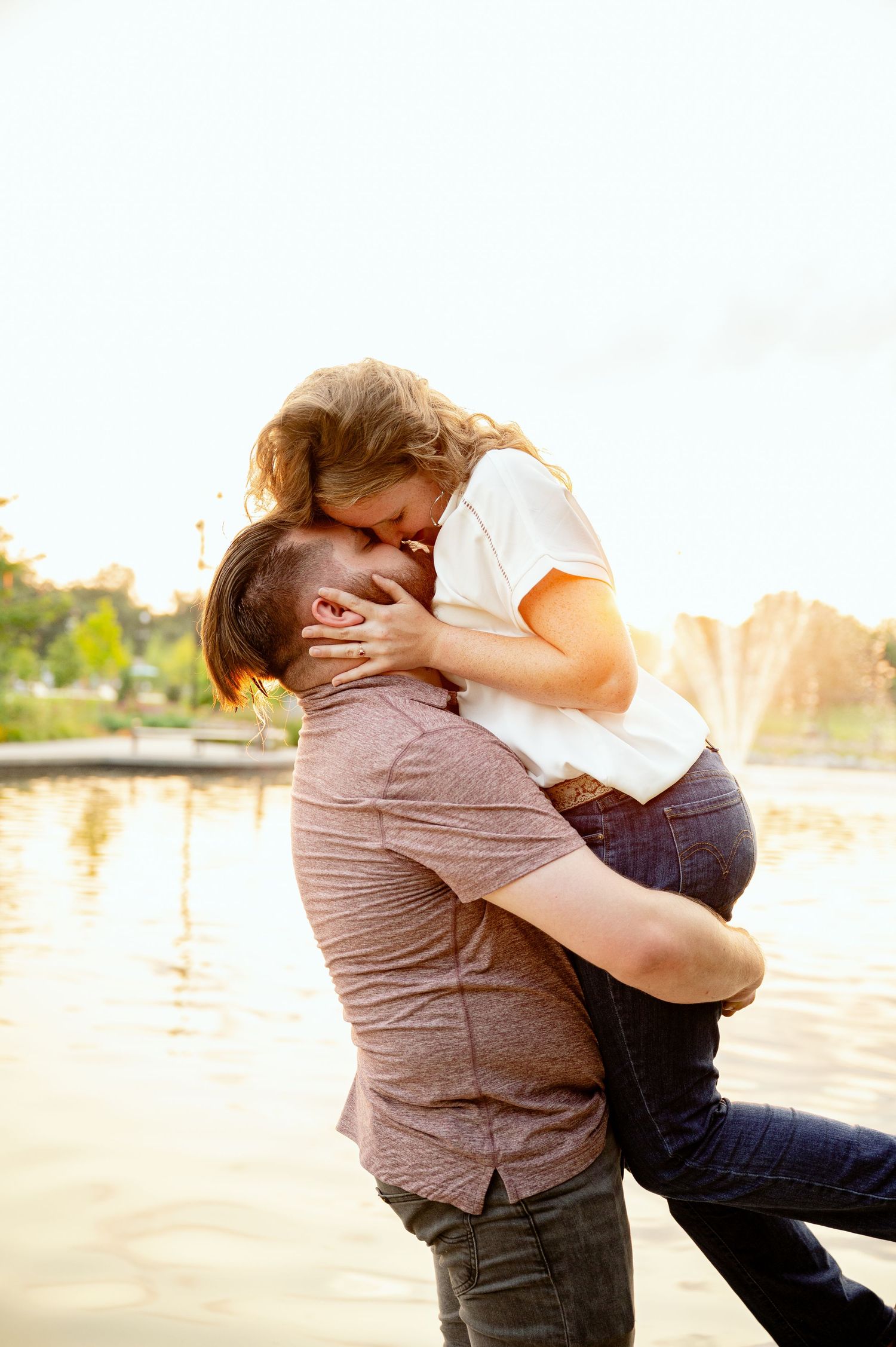 St cloud area engagement photographers photo couple shares a romantic embrace near a sunlit lake during an outdoor engagement photo session.