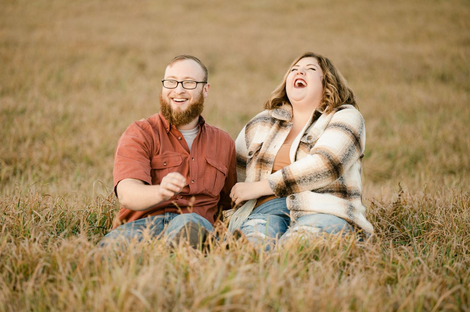 A couple sits in a grassy field with their smiling dog during a warm autumn photoshoot. St cloud area engagement photos.