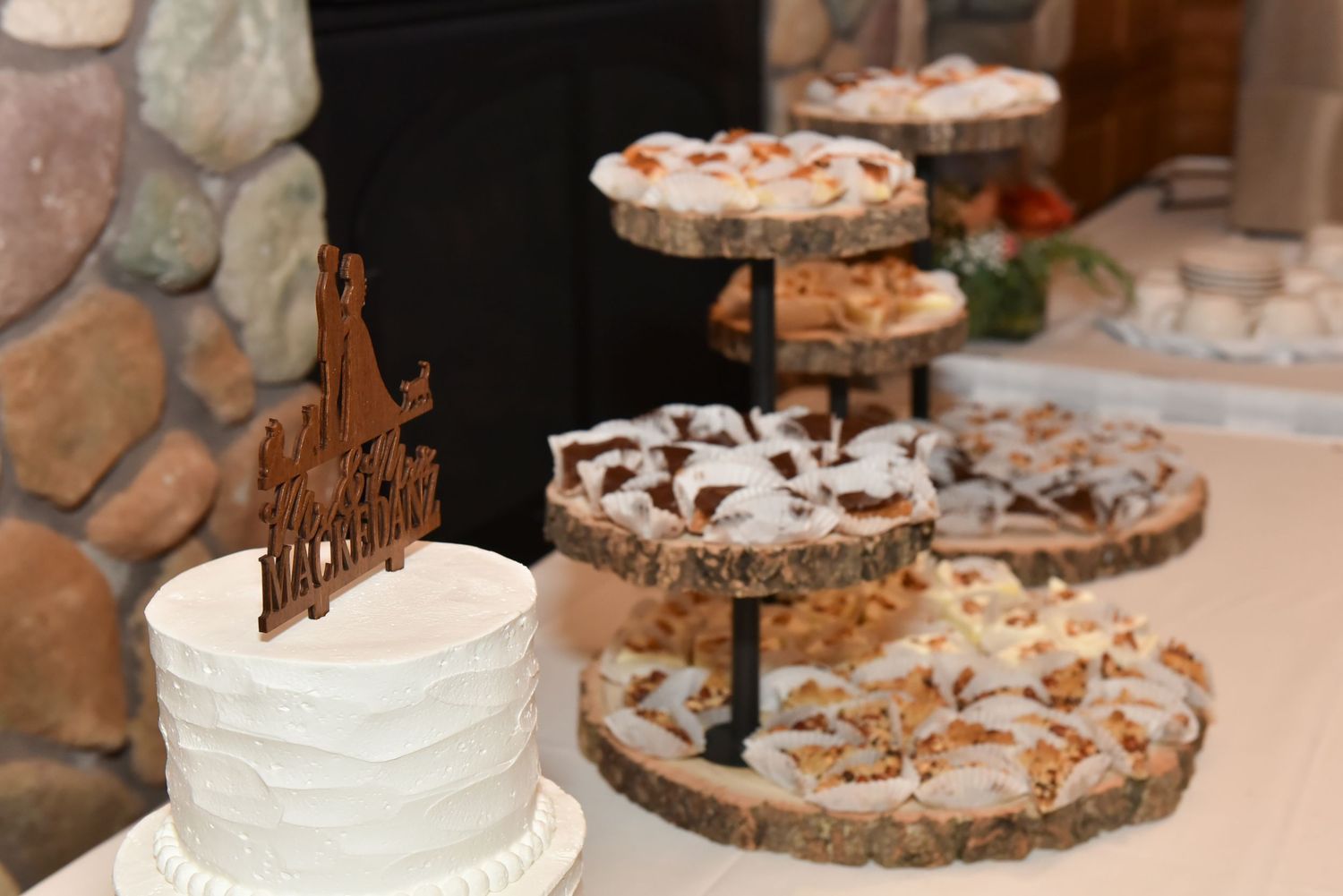 Wedding dessert table featuring white wedding cake and various pastries on rustic wooden displays.