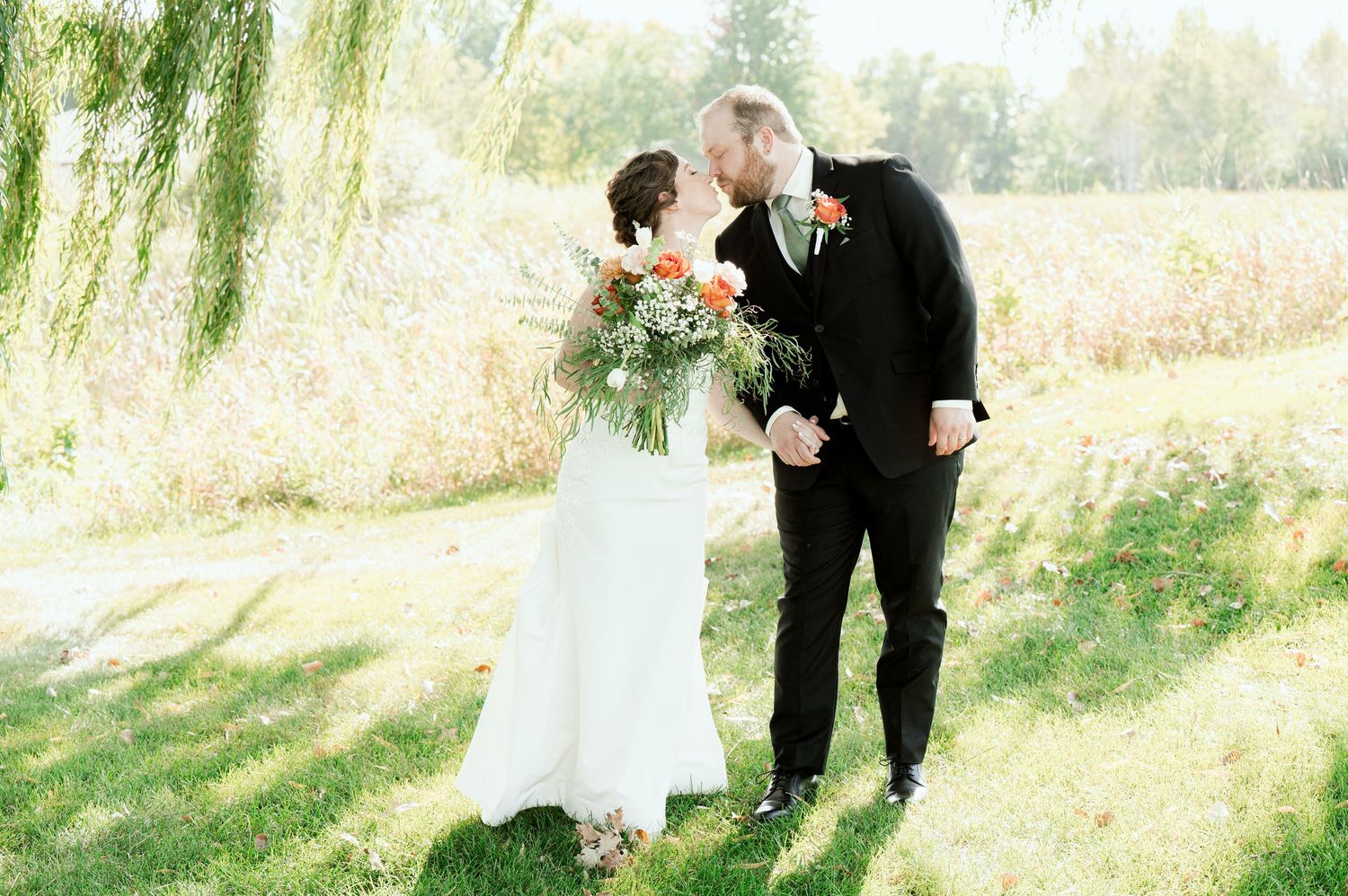 Elegant outdoor wedding ceremony under willow trees with a floral arrangement on a table.
