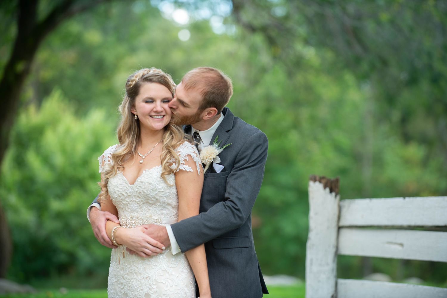 Intimate moment between couple in wedding attire by white fence. Rum River Barn Milaca Minnesota Weddings