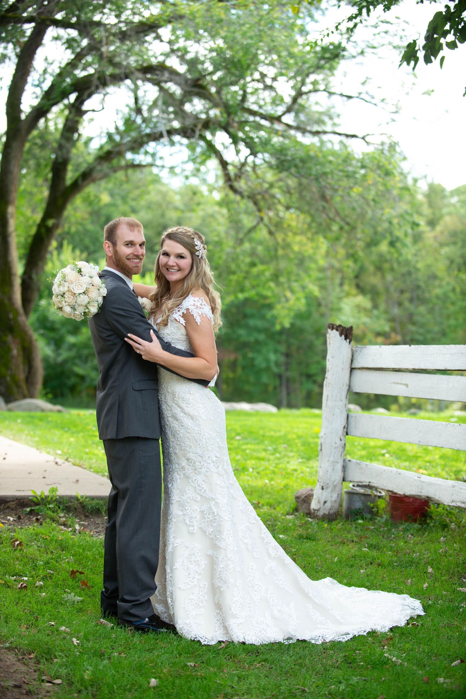 Newlyweds share intimate moments during their outdoor photo session near a white fence. Rum River Barn Milaca Minnesota Weddings