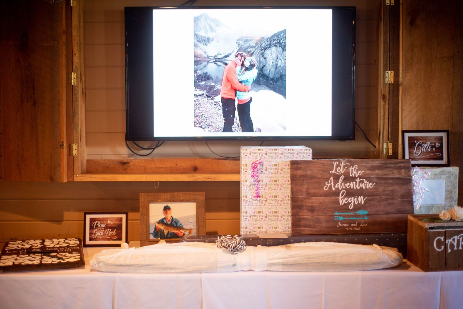 Wedding reception display with engagement photo projected above dessert table and wooden decor boxes.