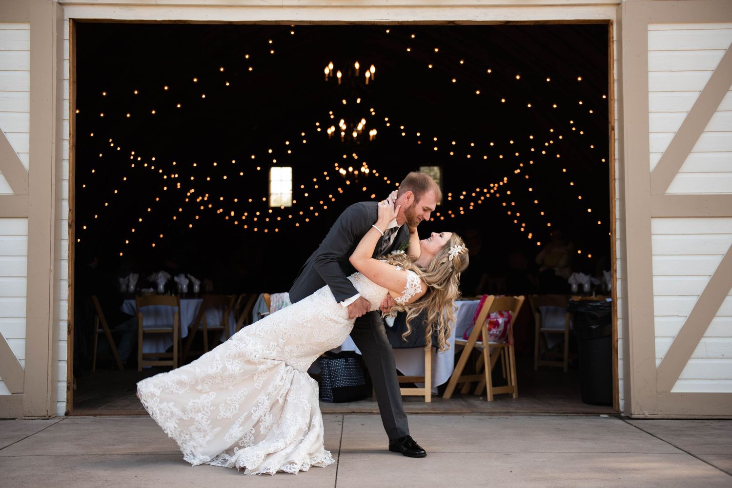 A romantic dip pose is performed in a barn doorway under twinkling lights. Rum River Barn Milaca Minnesota Weddings