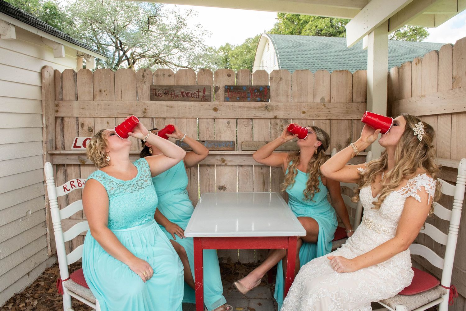 Four bridesmaids in mint dresses and white dress share laughs while drinking from decorative straws on a porch. Rum River Barn Milaca Minnes