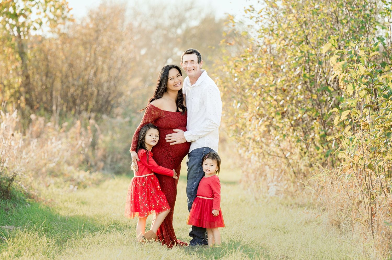 Family in coordinating red outfits poses together in autumn field.