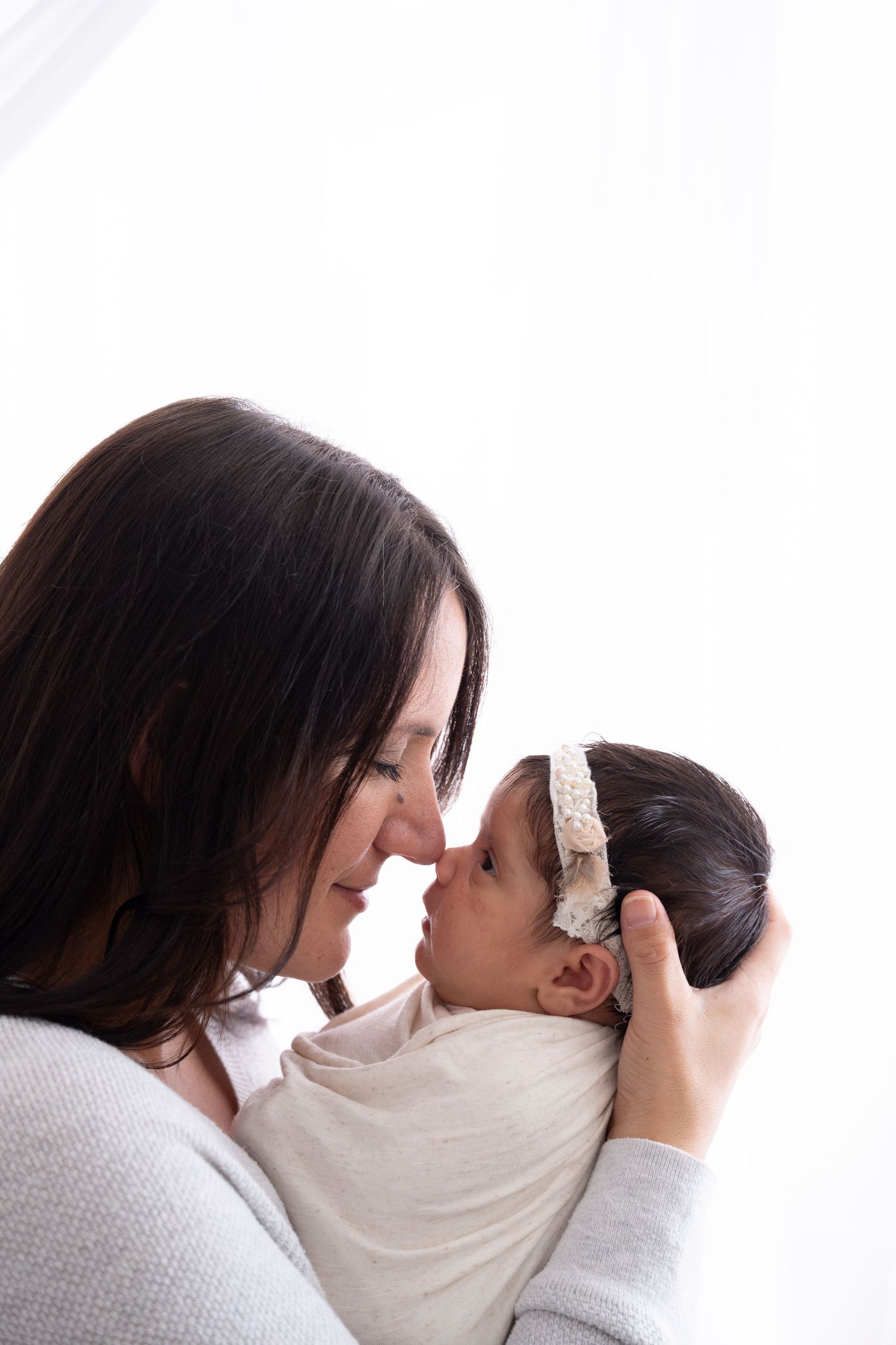 Tender moment between mother and newborn against white backdrop.