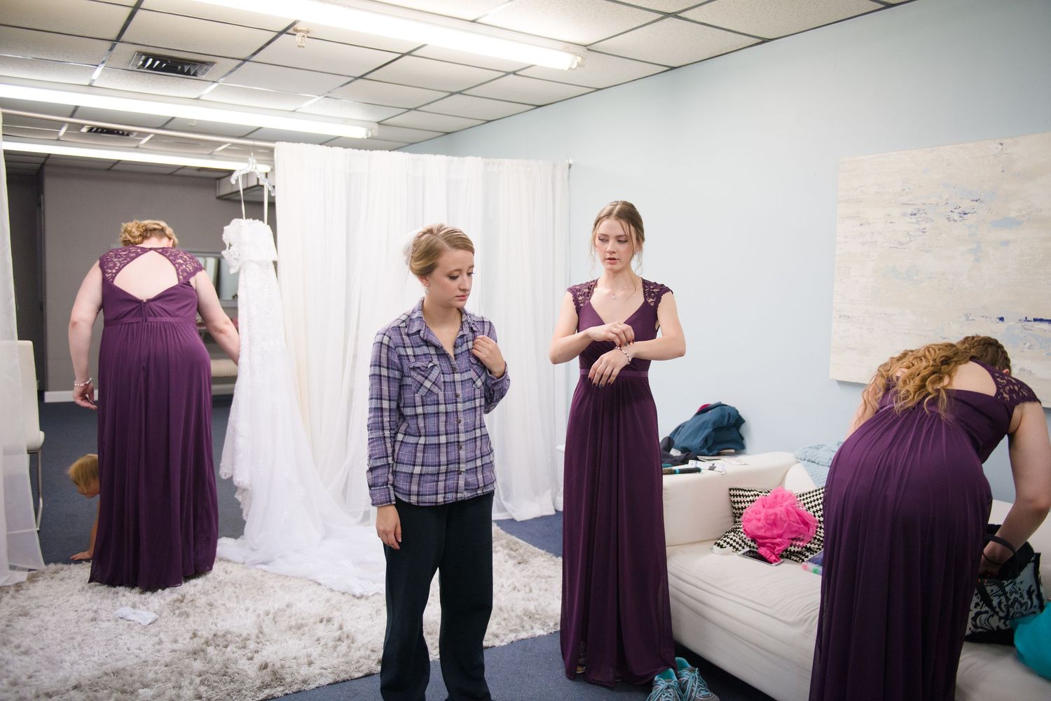 Wedding preparation scene with people in purple dresses gathered in a room with white walls. Andover wedding at Magestic Oaks Golf Club