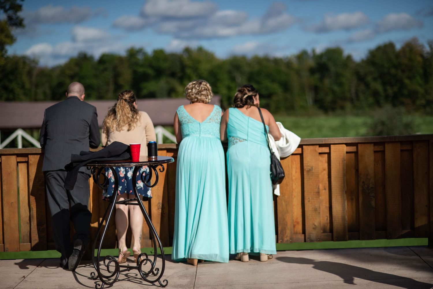Wedding guests gather on a wooden deck overlooking scenic countryside views.