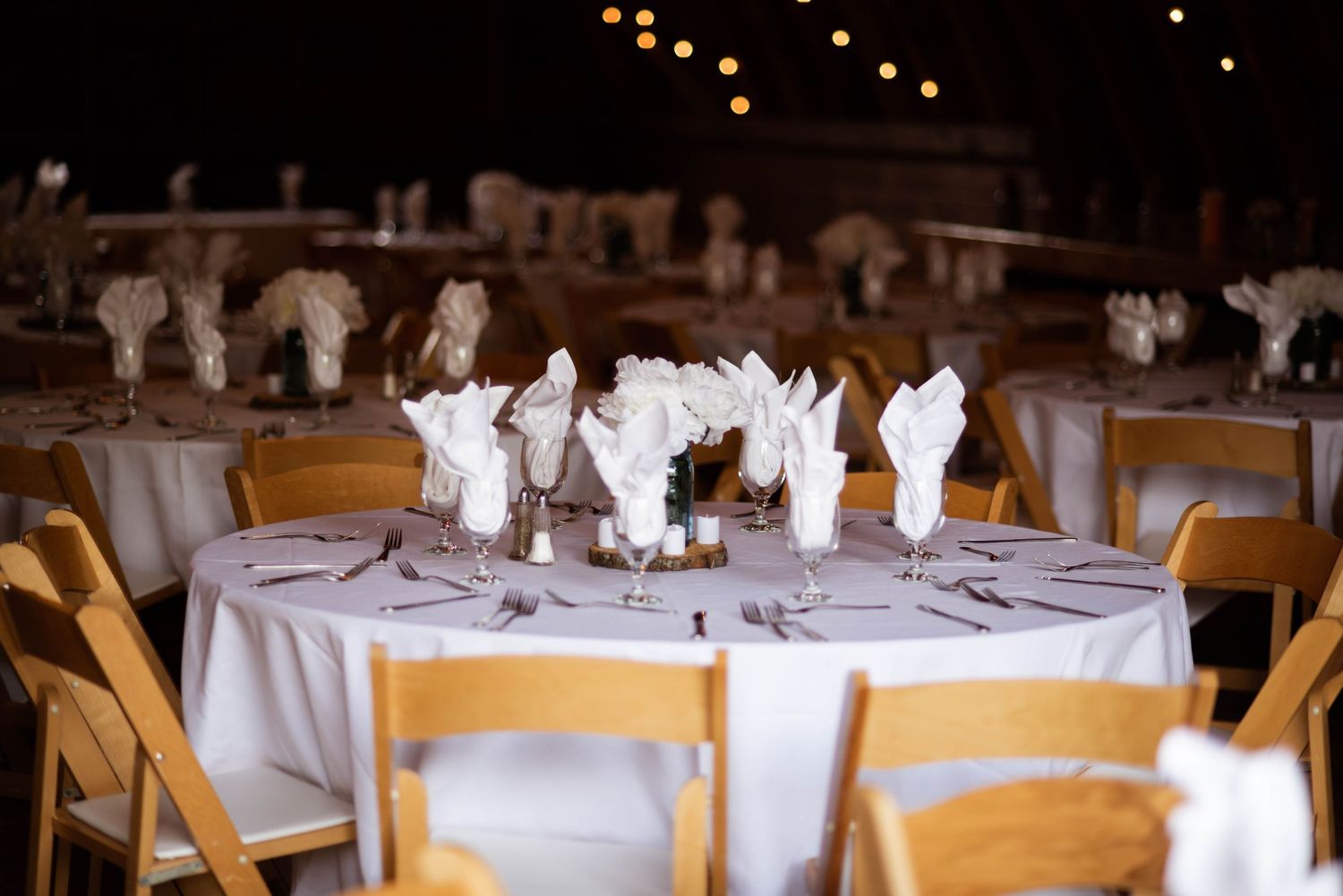 White tablecloths and gold chairs are elegantly arranged in a rustic reception venue with warm ambient lighting.
